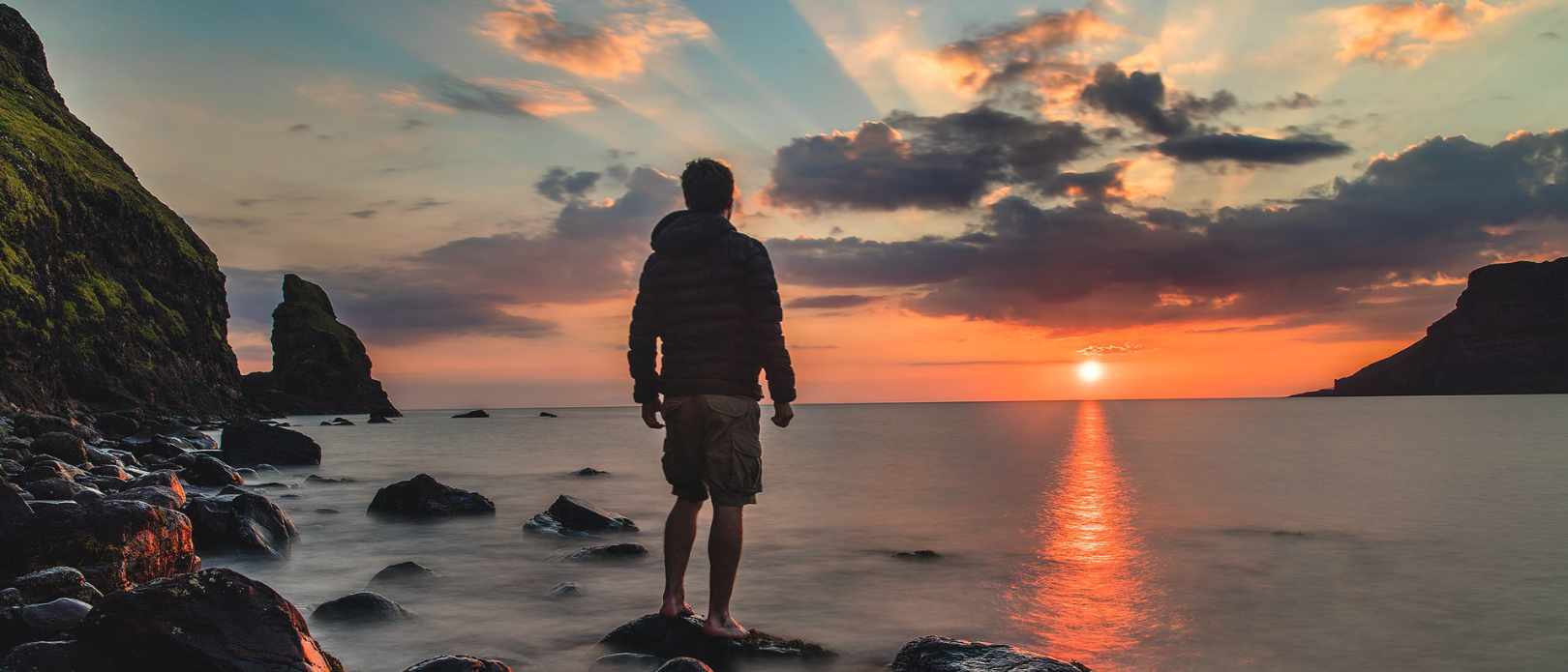 Man standing on stone looking at sunset by sea